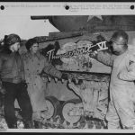 Lt. Col. Creighton Abrams (right), commander of the 37th Tank Battalion, 4th Armored Division, points to the name “Thunderbolt VI” on his Sherman tank after the breakthrough to Bastogne, Belgium. Capt. McIntire and Capt. Brueland stand with him. January 1945.