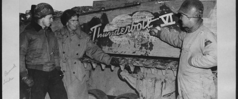 Lt. Col. Creighton Abrams (right), commander of the 37th Tank Battalion, 4th Armored Division, points to the name “Thunderbolt VI” on his Sherman tank after the breakthrough to Bastogne, Belgium. Capt. McIntire and Capt. Brueland stand with him. January 1945.